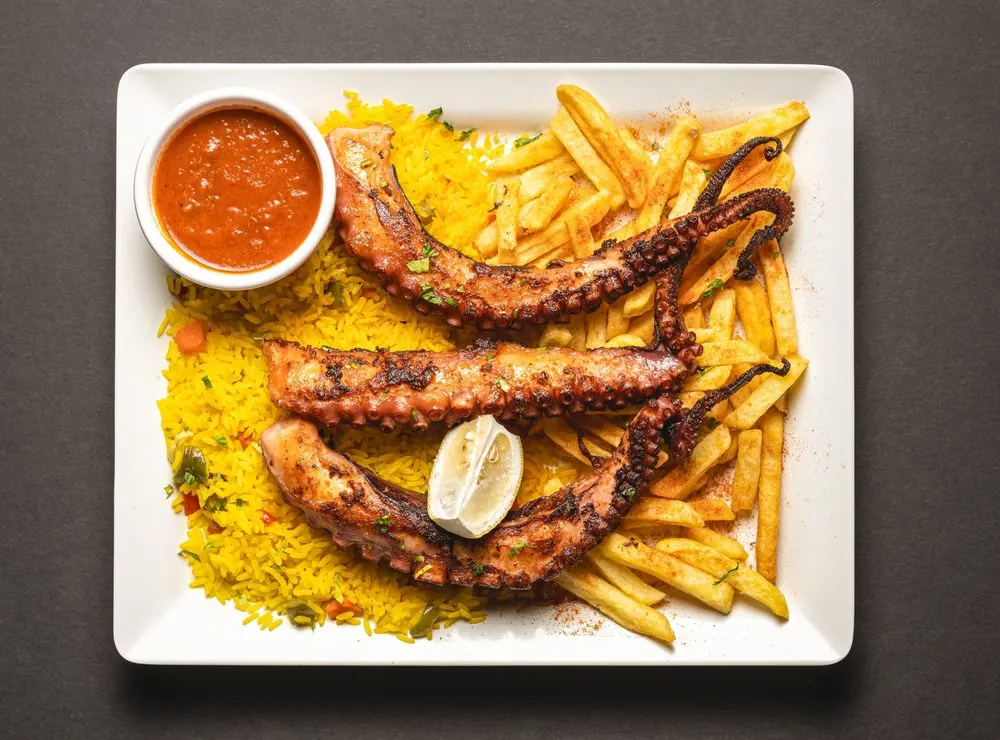 Grilled octopus tentacles over yellow rice and chips