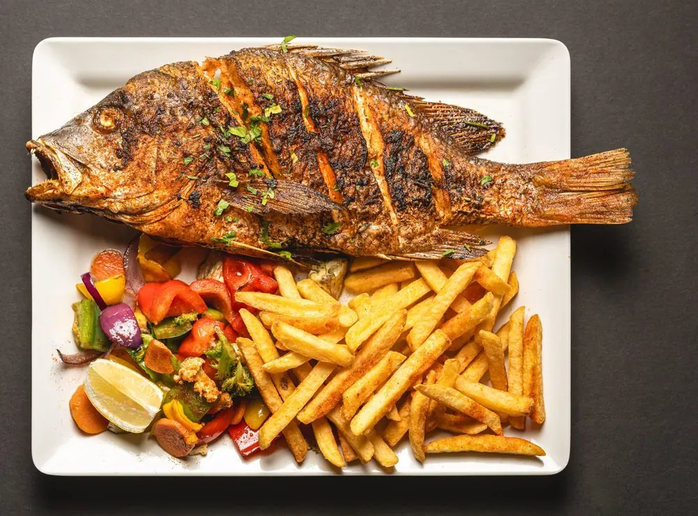 A whole king size snapper with chips and grilled vegetables