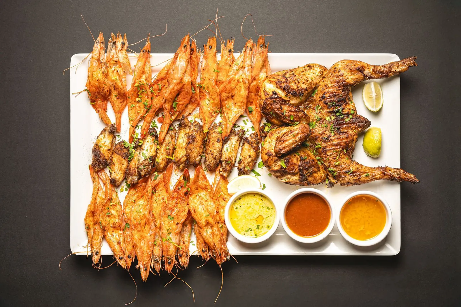 A Shrimp & Co. shrimp platter with three dips on a dark slate table
